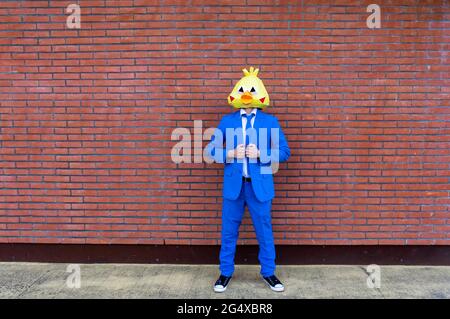 Man wearing vibrant blue suit and bird mask standing in front of brick wall