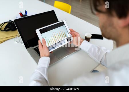 Male entrepreneur checking graph on digital tablet while working at office Stock Photo