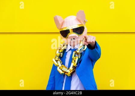 Man wearing vibrant blue suit, pig mask and large golden chain pointing toward camera Stock Photo