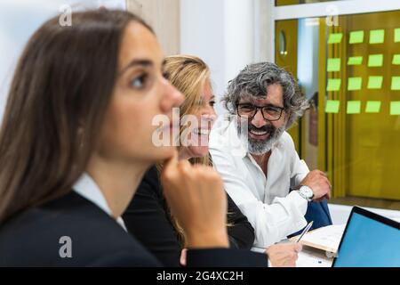 Happy male and female professionals smiling by businesswoman contemplating at office Stock Photo