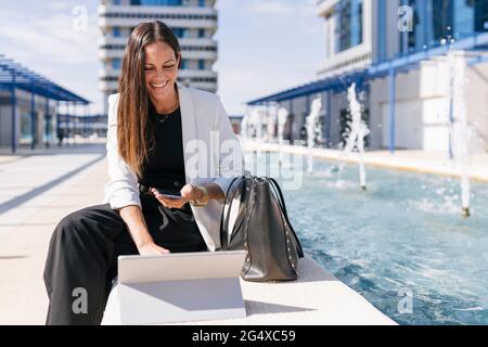 Businesswoman with digital tablet using mobile phone during sunny day Stock Photo