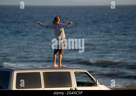 Carefree man standing with arms outstretched on mini van roof Stock Photo