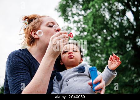 Mother blowing bubbles with son at park Stock Photo