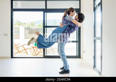 Cheerful boyfriend carrying girlfriend while standing in new home Stock Photo