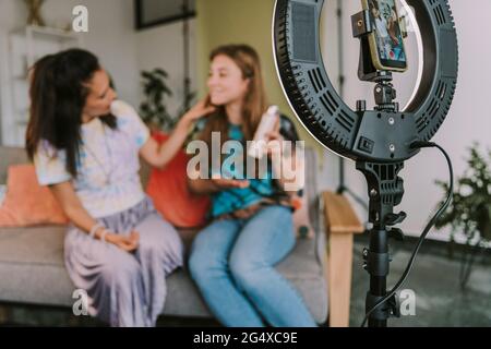 Female influencers vlogging through ring light and smart phone at home Stock Photo