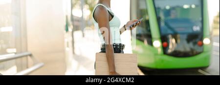Woman holding smart phone while tram arriving at tram station Stock Photo