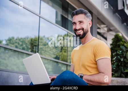 Smiling businessman looking away while sitting with laptop Stock Photo