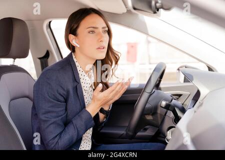 Worried businesswoman talking on call while gesturing in car Stock Photo