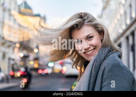 Smiling beautiful blond woman tossing hair while standing in city Stock Photo