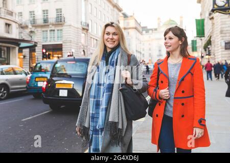 Smiling young women walking together on sidewalk Stock Photo