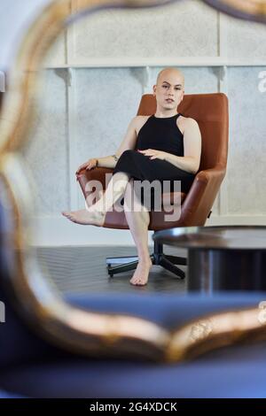 Transgender woman in black dress sitting on chair at home Stock Photo