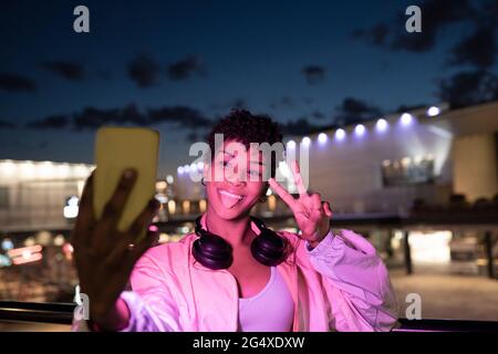 Young woman taking selfie through smart phone while making positive emotions at night Stock Photo