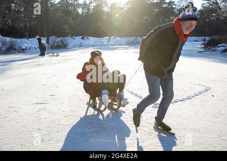 Senior man with young couple pulling on sled while ice skating over frozen lake Stock Photo
