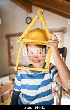 Boy smiling while holding house of measuring tape at attic Stock Photo