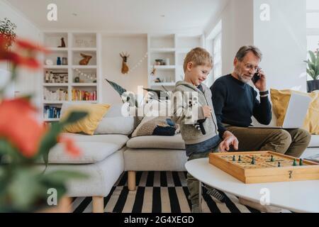 Man talking on mobile phone while playing ludo game with son at home Stock Photo