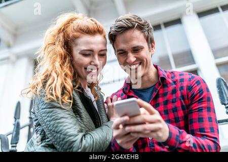 Smiling couple using smart phone at street Stock Photo