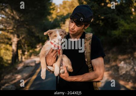 Young male hiker standing with backpack and pet in forest Stock Photo