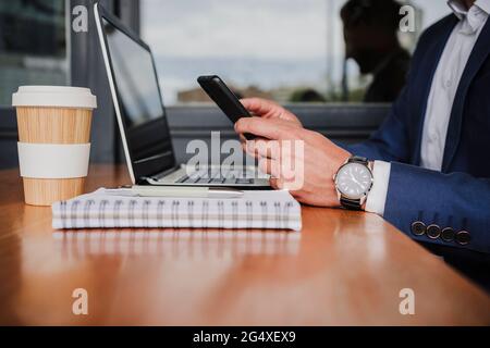 Businessman with laptop using mobile phone at cafeteria Stock Photo