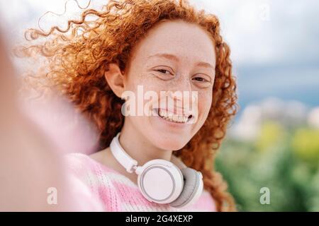 Cheerful young woman with curly hair wearing headphones Stock Photo