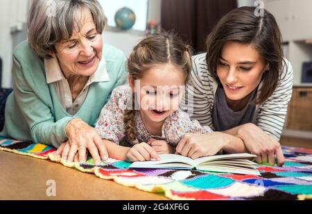 Girl reading book while lying by women in nursery Stock Photo