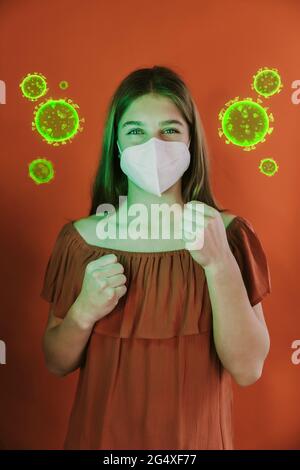 Girl wearing protective face mask standing in fighting stance amidst coronavirus over red background Stock Photo