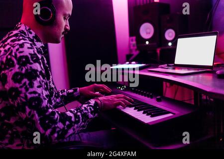Young man wearing headphones playing piano while composing music at studio Stock Photo