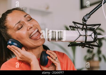 Female singer with headphones singing on microphone at home Stock Photo