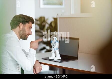 Male entrepreneur pointing at robot on laptop at office Stock Photo