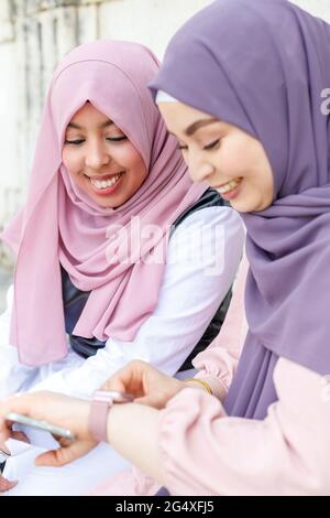 Smiling woman adjusting smart watch while sitting by female friend Stock Photo