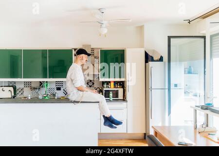 Young man looking away while sitting on kitchen island at home Stock Photo