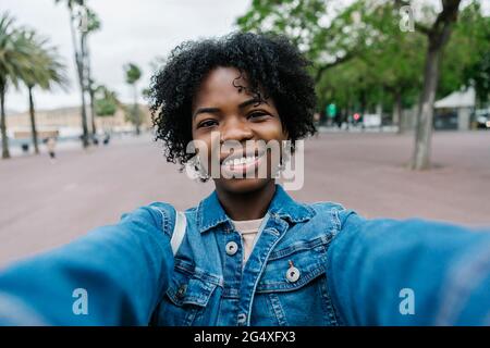 Smiling young woman with Afro hairstyle taking selfie Stock Photo
