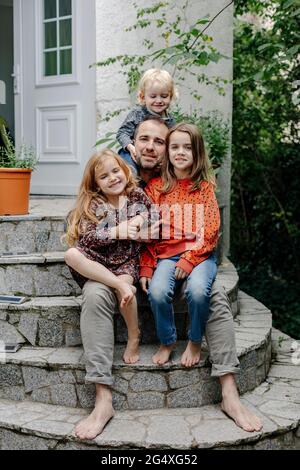 Father sitting with daughters and son on steps at entrance of house Stock Photo