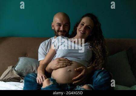 Man sitting with hands on pregnant woman's abdomen in bedroom Stock Photo