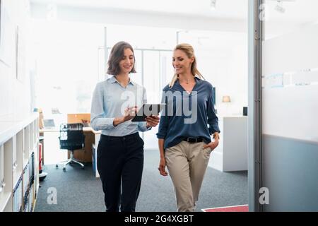 Female coworkers discussing over digital tablet while walking in office Stock Photo