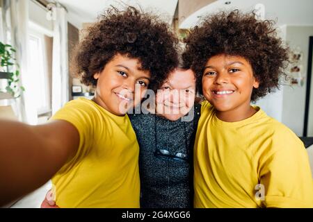 Smiling twin boys standing together with great grandmother at home Stock Photo