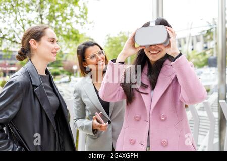 Smiling businesswoman using virtual reality headset while standing by colleagues Stock Photo