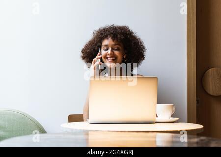 Female university student talking on mobile phone while sitting at cafe Stock Photo