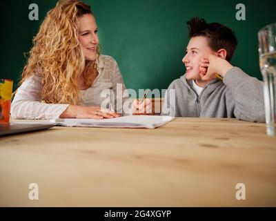 Smiling blond woman teaching son at home Stock Photo