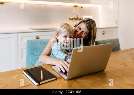 Smiling boy using laptop with mother working at home Stock Photo