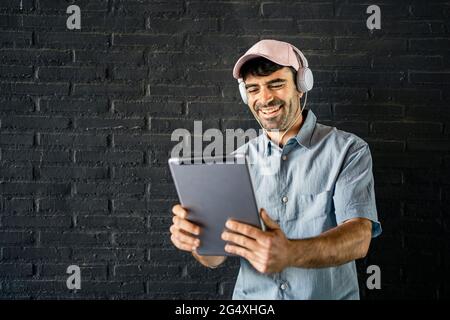 Happy young man using digital tablet in front of wall Stock Photo