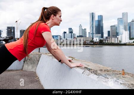 Active sportswoman doing warm up exercise over retaining wall in city Stock Photo