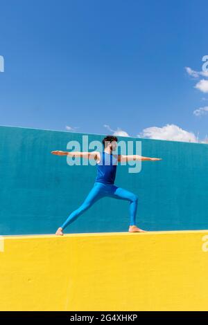 Man practicing Virabhadrasana II while doing yoga on retaining wall Stock Photo