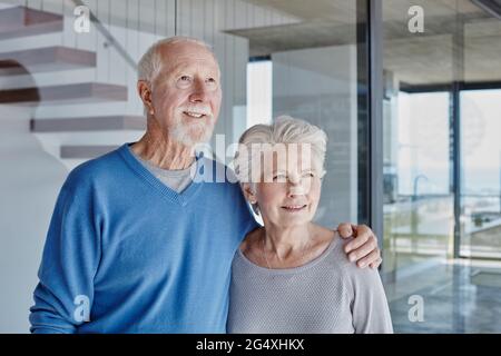 Smiling senior couple standing together in front of glass wall Stock Photo