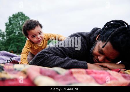 Worried son looking at father lying on picnic blanket at park Stock Photo