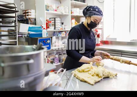 Female baker with rolling pin and dough in commercial kitchen at bakery Stock Photo