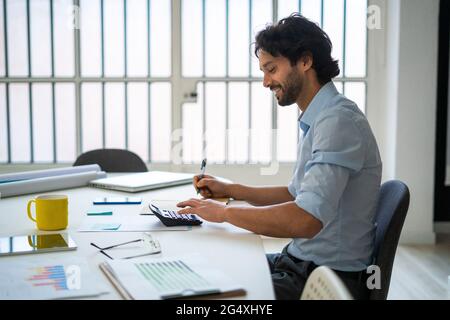 Smiling young businessman working while sitting by desk in office Stock Photo