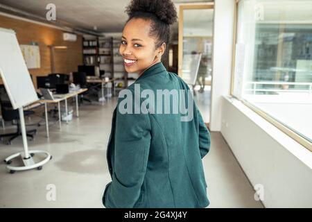 Businesswoman smiling while looking over shoulder at office Stock Photo