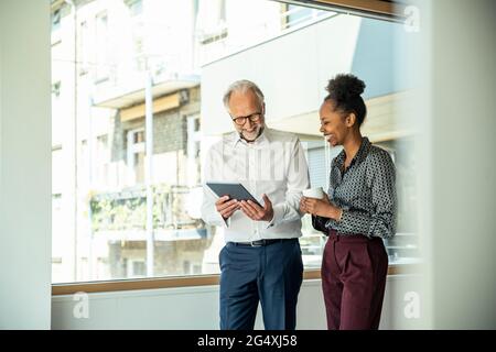 Smiling male and female colleagues looking at digital tablet while standing in office Stock Photo