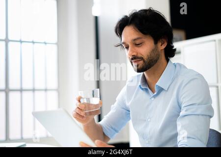 Businessman with drinking glass using digital tablet in office Stock Photo