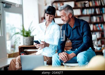 Businesswoman using mobile phone while sitting by colleague at cafe Stock Photo
